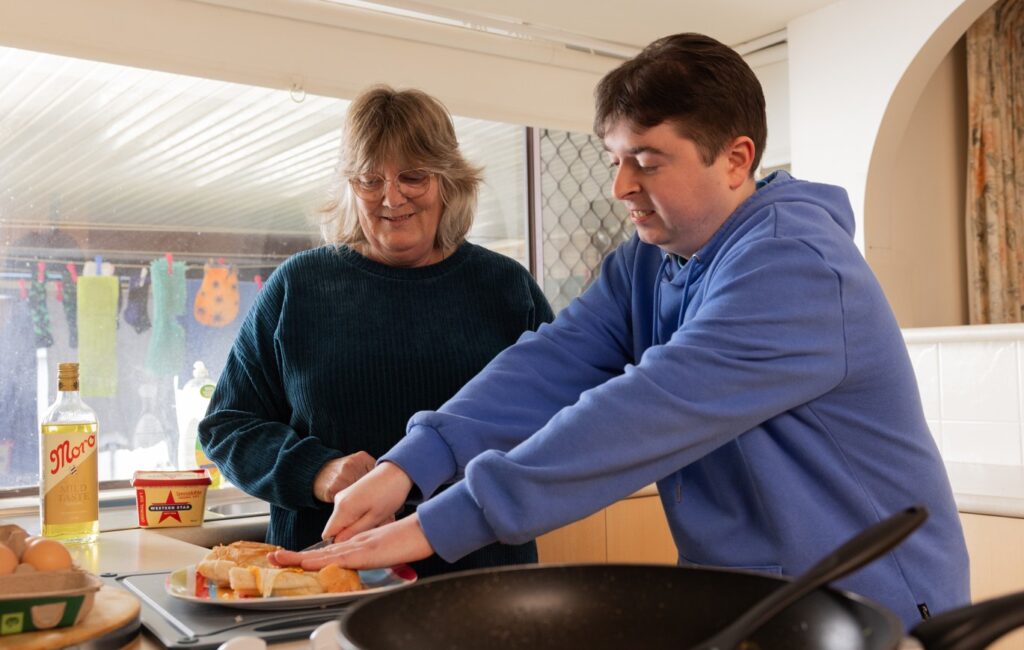 Supported Independent Living Client Jesse cooking in his kitchen with a Support Worker.