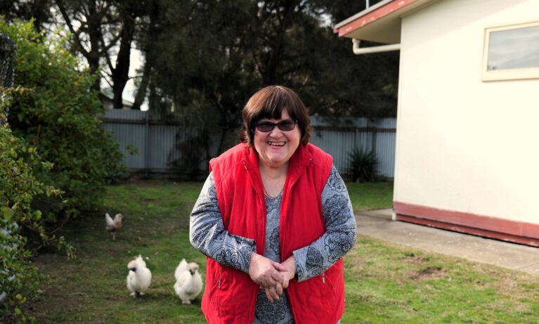 Supported Independent Living Client smiling in her backyard in front of chickens.