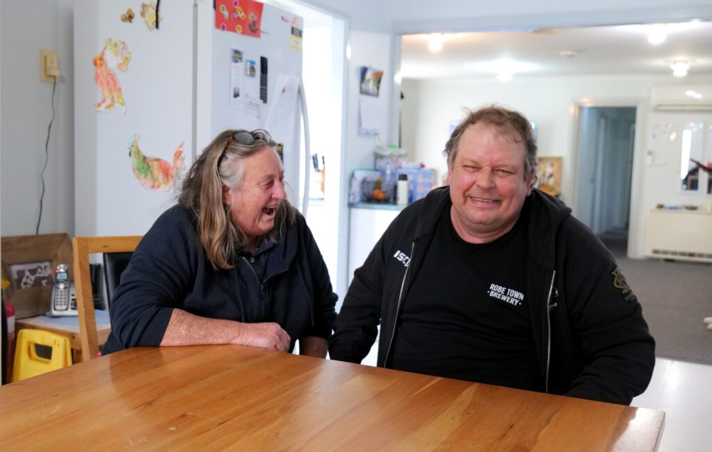 Support Worker and Supported Independent Living Client sitting at a kitchen table laughing.