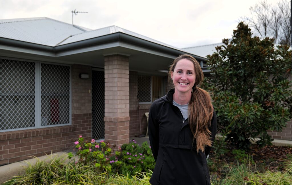 Support Worker smiling in front of a house where she provides Supported Independent Living services for Clients.