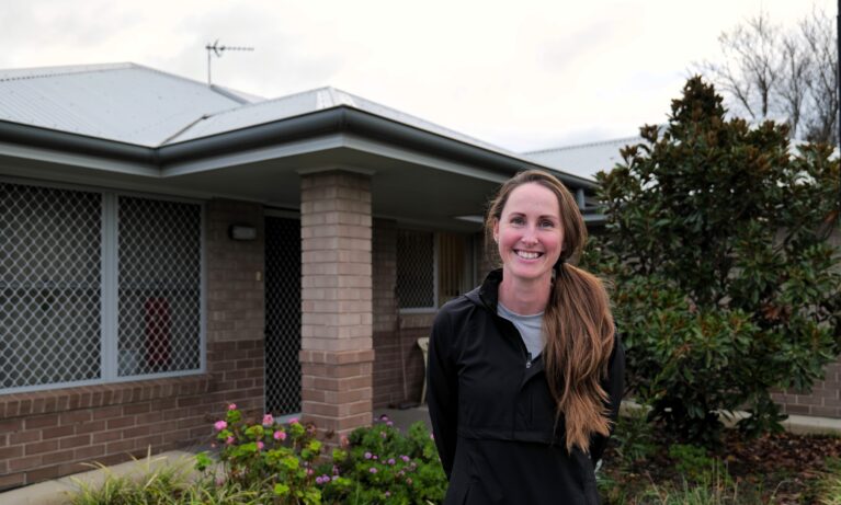 Support Worker smiling in front of a house where she provides Supported Independent Living services for Clients.