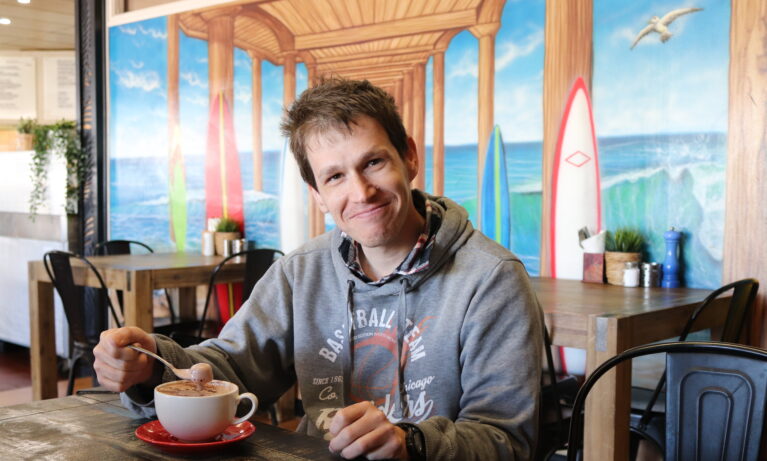 Individual Support Client sitting in a cafe smiling with a cappuccino.